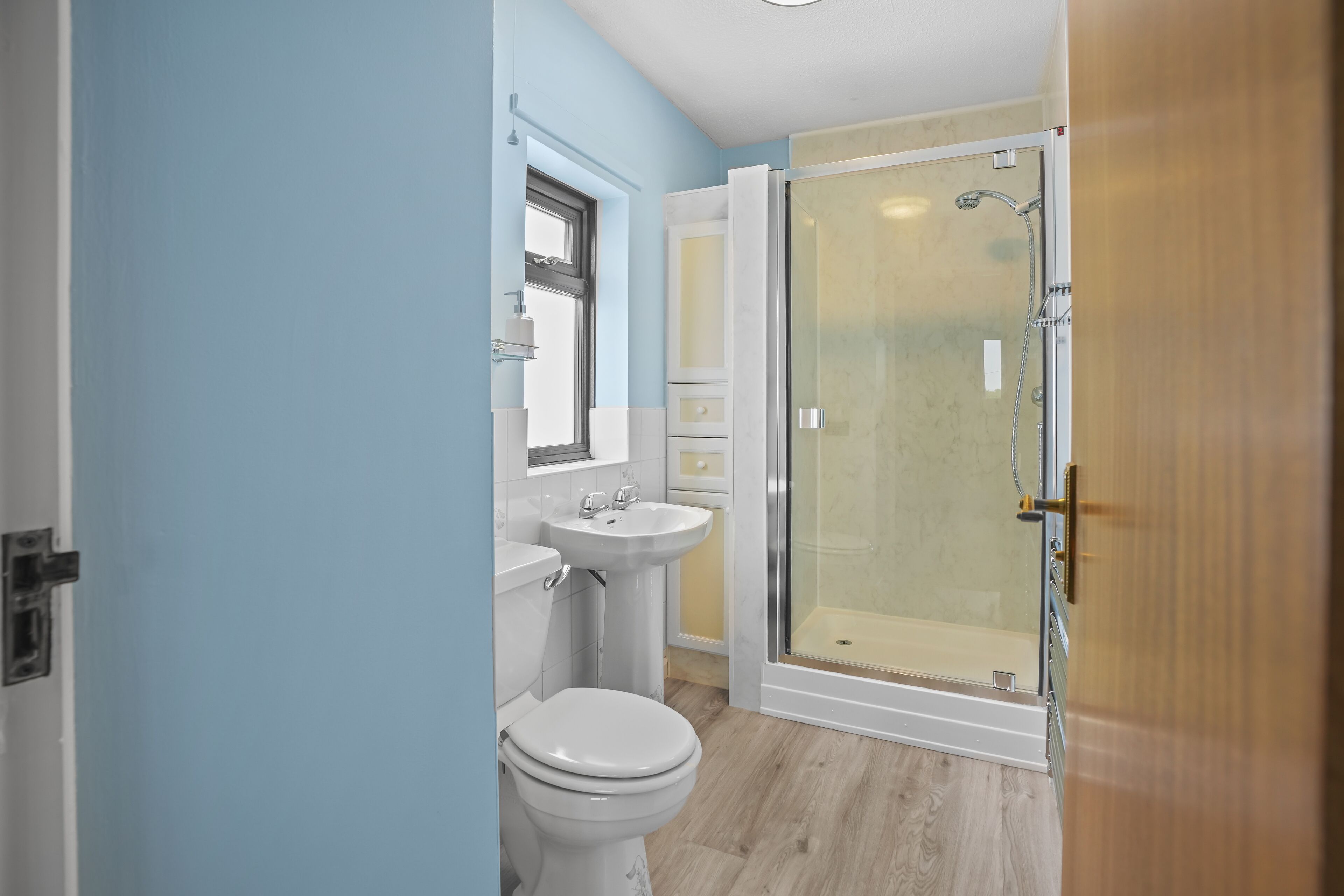 Une salle de bain comprenant des toilettes, un lavabo et une douche fermée par des parois en verre.