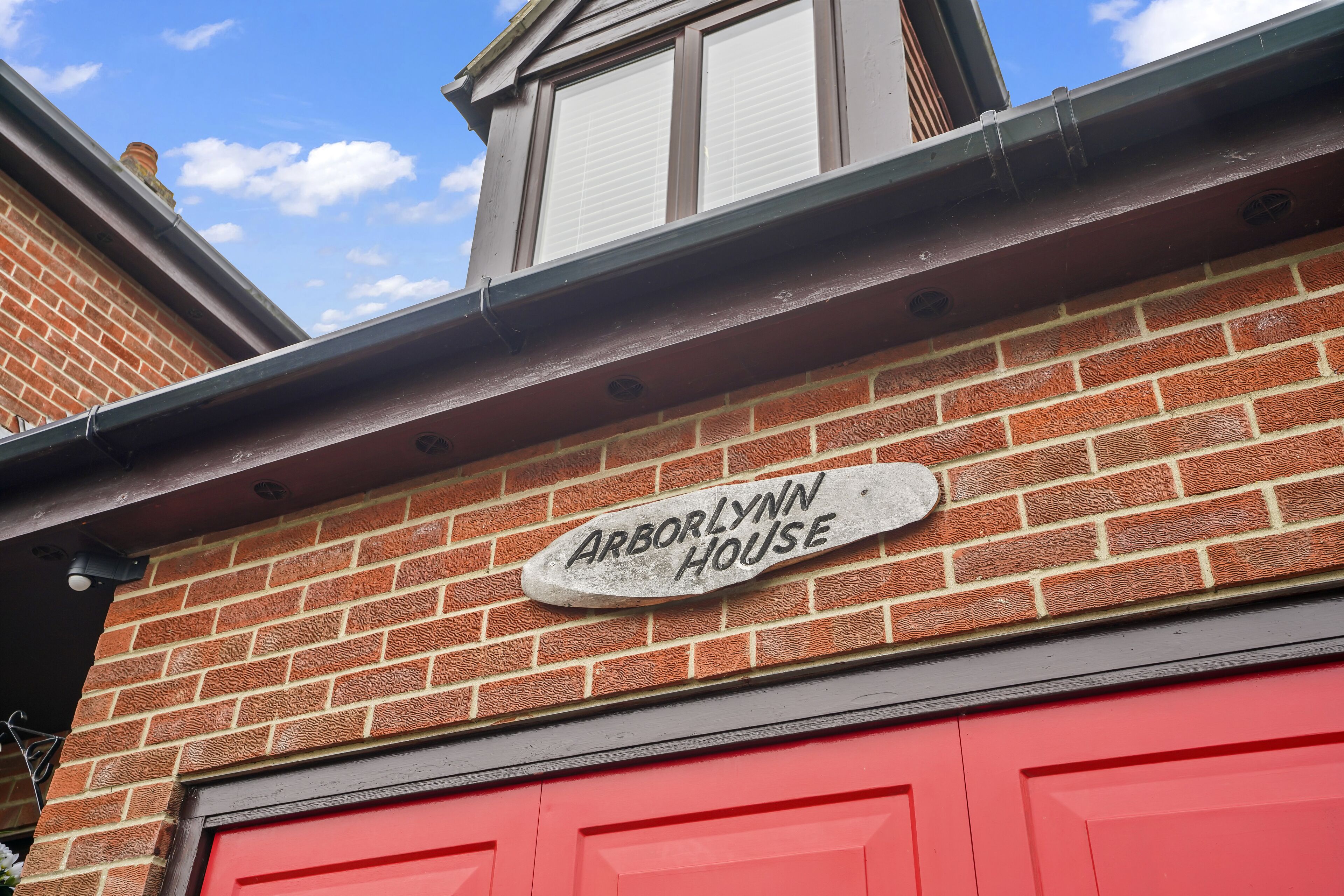 Une maison en briques avec une porte de garage rouge et une enseigne en pierre sur laquelle on peut lire « Arborynn House ».