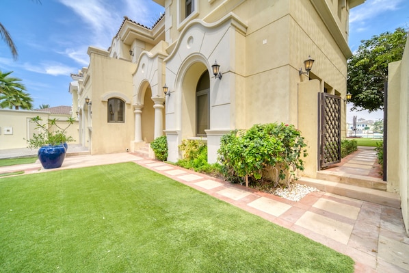 A Mediterranean-style building with a well-maintained lawn, a stone pathway, and a decorative gate.
