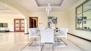 A spacious dining area with a long table, white chairs, and a chandelier.