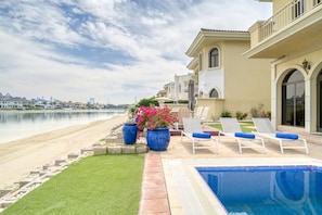 A pool area with a view of the beach, lounge chairs, and a large planter with flowers. - Premier 6BR Villa with Assistant's Room and Private Pool in Frond E Palm Jumeirah by Deluxe Holiday Homes (Dubai)