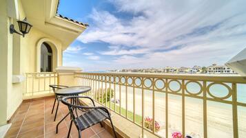 A balcony with a table and chairs, a railing, and a view of the beach and distant buildings.