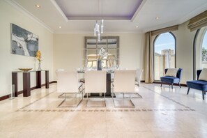 A spacious dining area with a modern chandelier, a large mirror, and a view through a window. - Premier 6BR Villa with Assistant's Room and Private Pool in Frond E Palm Jumeirah by Deluxe Holiday Homes (Dubai)