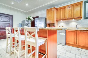 Eine Küche mit Holzausstattung, einem Edelstahlkühlschrank, einer Spülmaschine und einer Bar mit weißen Stühlen.