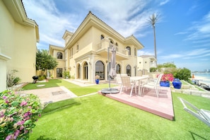 Una casa grande de dos pisos con un patio, mobiliario exterior y vista al océano.