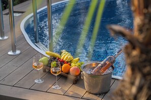 Una terrazza in legno con una vasca idromassaggio, un cesto di frutta e due bicchieri di vino.