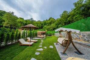 Un giardino curato con un muro in pietra, un gazebo con tetto di paglia e una sedia a dondolo.