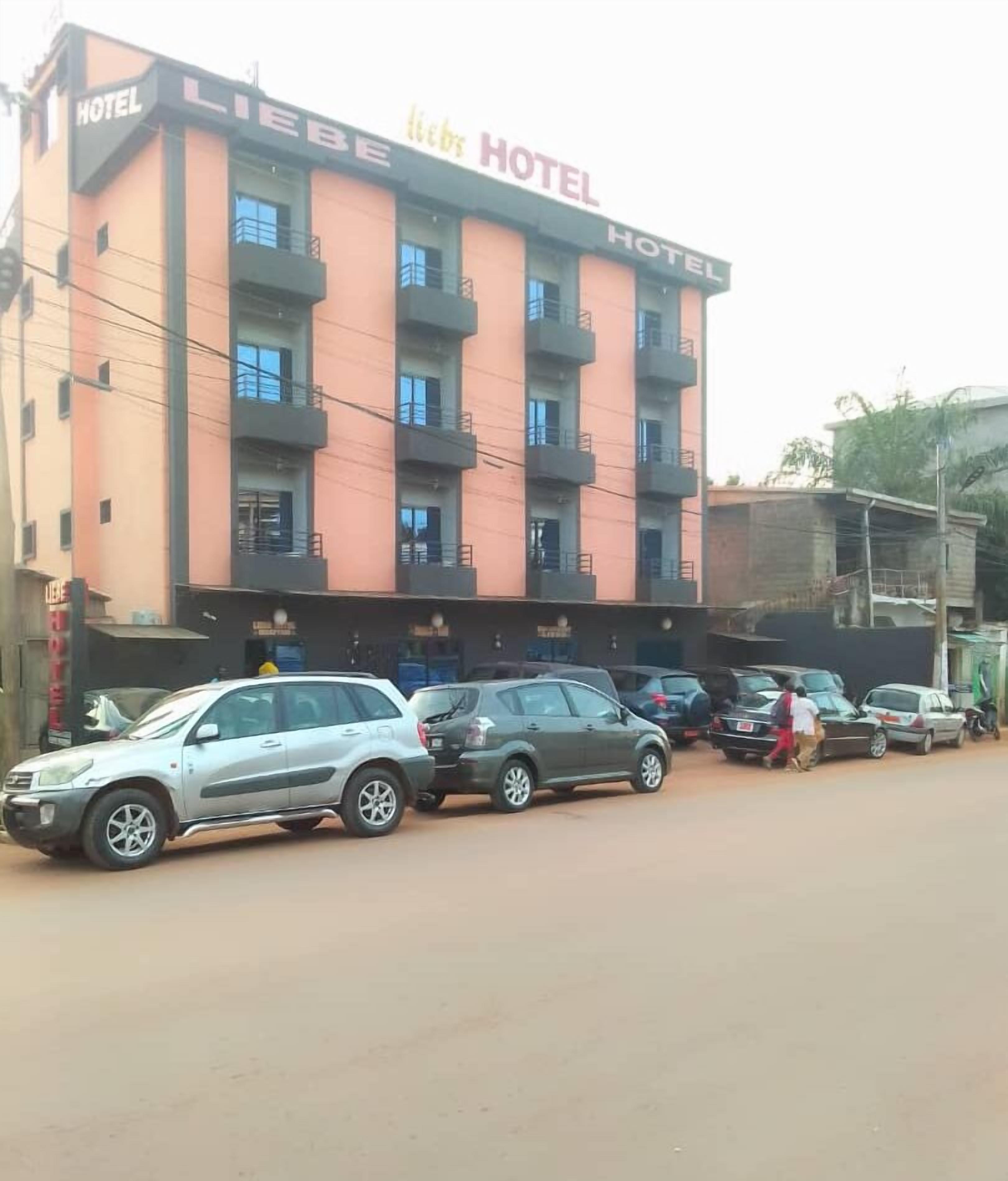 Un hotel con un edificio de varios pisos, balcones y un estacionamiento con varios automóviles.