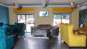 A lobby with teal and yellow armchairs, a grey sofa, and a television screen. - LIEBE HOTEL (Yaoundé)