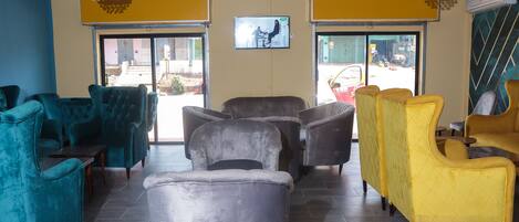 A lobby with teal and yellow armchairs, a grey sofa, and a television screen.