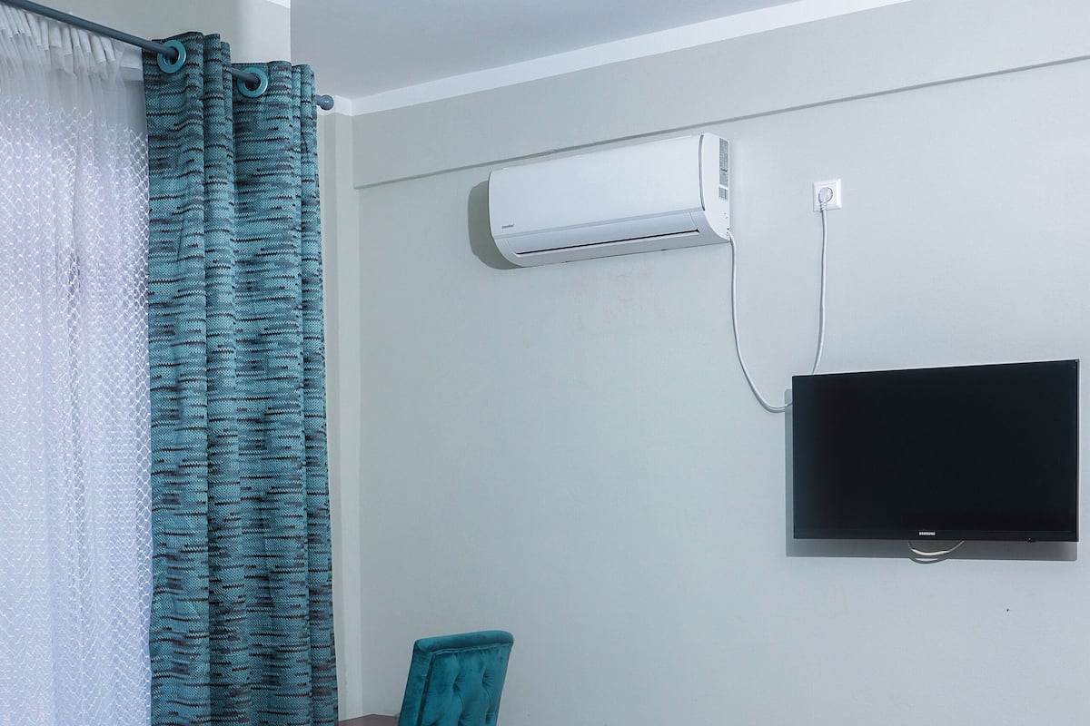 Un dormitorio con una cama, una silla, un televisor y un equipo de aire acondicionado.