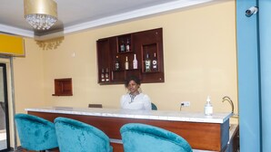 A bar area with a wooden counter, teal barstools, and a liquor cabinet above. - LIEBE HOTEL (Yaoundé)