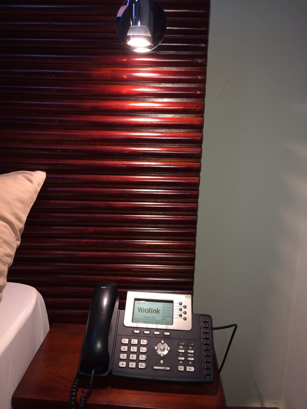 A Yealink phone on a wooden nightstand with a lamp above it.