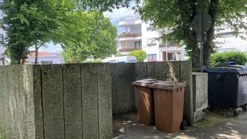 Udsigt over et boligområde med et træhegn, to brune skraldespande og en blå genbrugsbeholder.