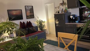 Een moderne woonkamer met een bank, een eettafel en een keuken met apparatuur.