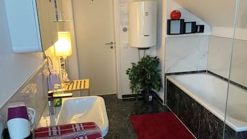 Et badeværelse med et hvidt badekar, et rødt håndklæde, en potteplante og en håndklædeholder.