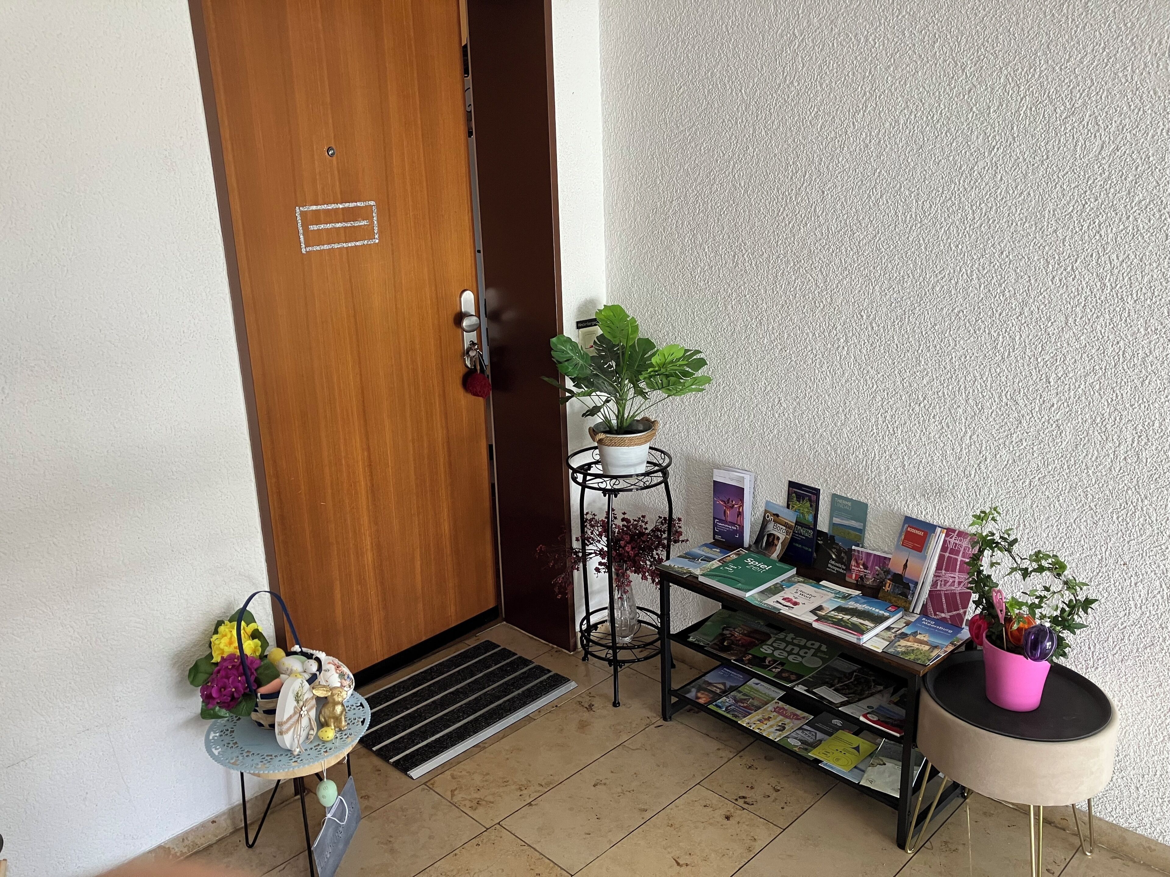 A room with a wooden door, a small table with a plant, a magazine rack, and a decorative item on the floor.