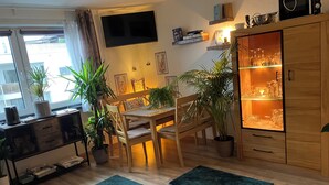Un salon moderne comprenant un coin repas, des meubles en bois, des plantes en pot et un téléviseur fixé au mur.