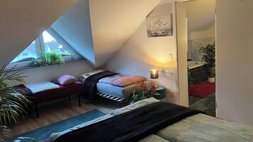 A bedroom with a bed, bedside table, lamp, and a window with plants.