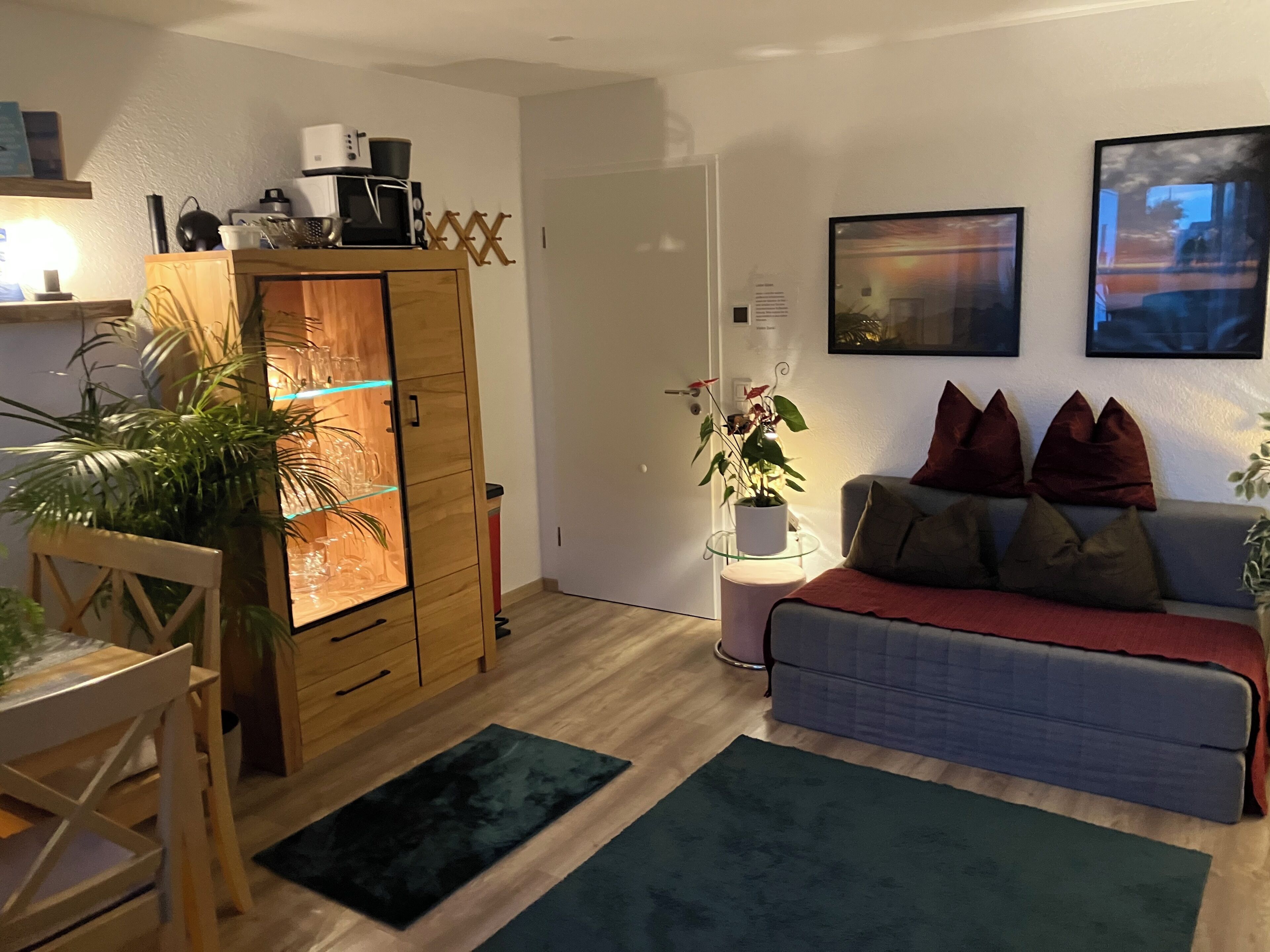 A living room with a wooden cabinet, a sofa, a dining table with chairs, and a potted plant.