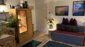 A living room with a wooden cabinet, a sofa, a dining table with chairs, and a potted plant.