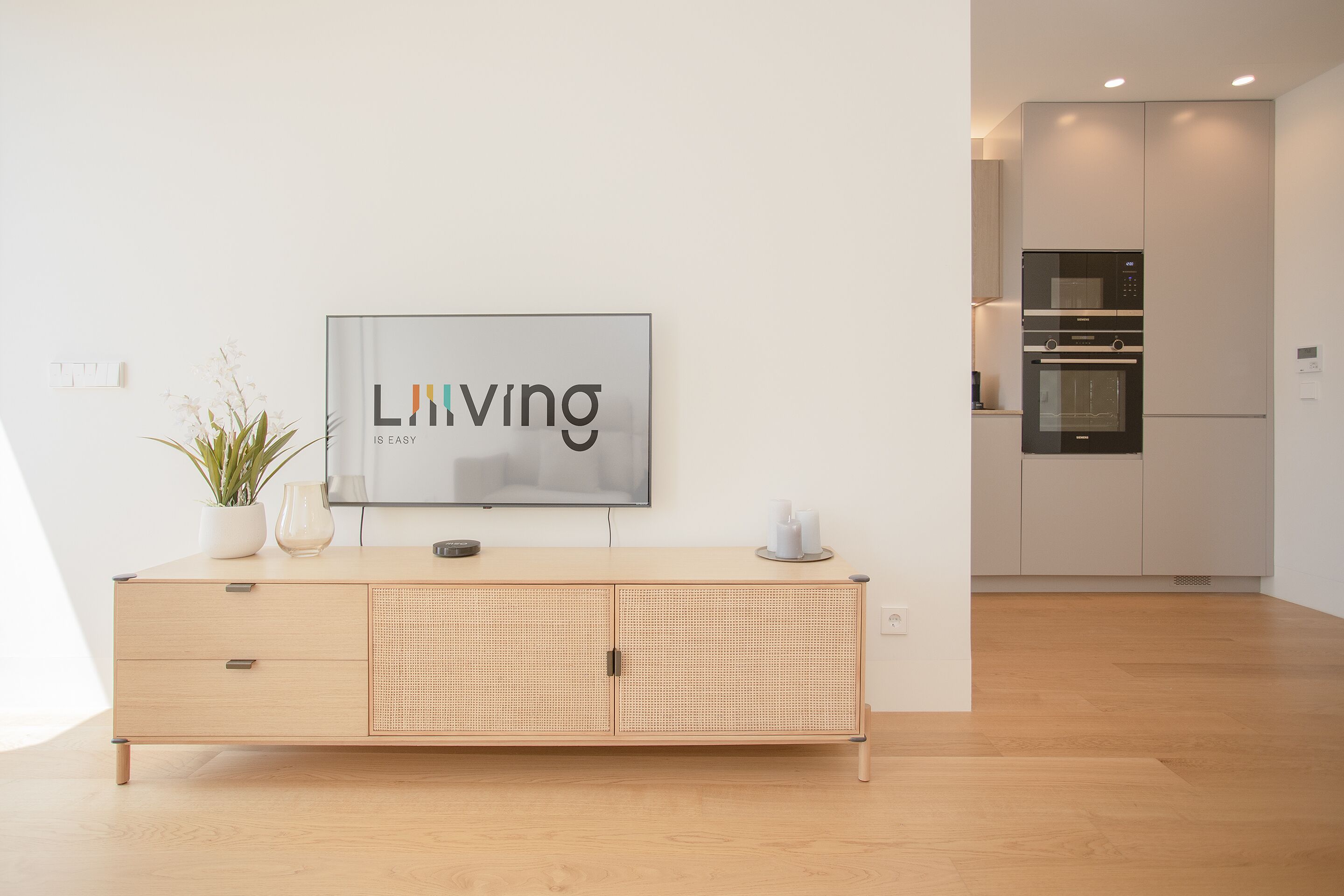 A modern kitchen with a built-in oven and microwave, a wooden cabinet with a plant, and a framed sign on the wall.