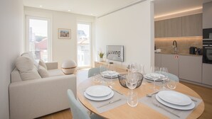 A modern living room with a dining area, a sofa, a TV, and a kitchen with a coffee machine. - Liiiving - Crystal Palace Apartment (Porto)