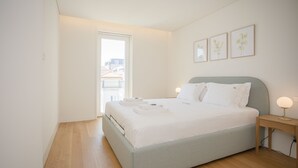 A bedroom with a bed, bedside table, and a window. - Liiiving - Crystal Palace Apartment (Porto)