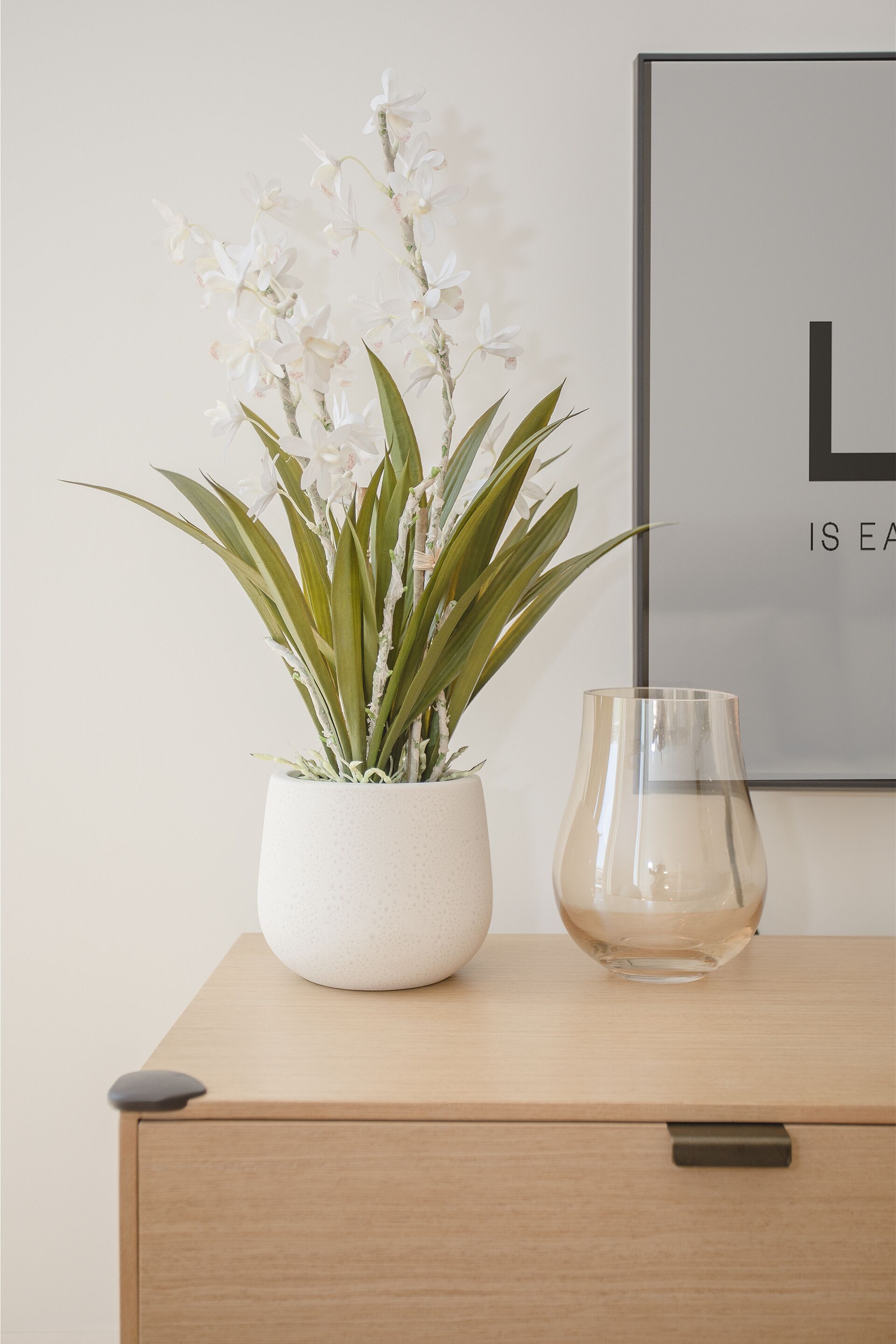 A wooden cabinet with a potted orchid and a clear glass vase.