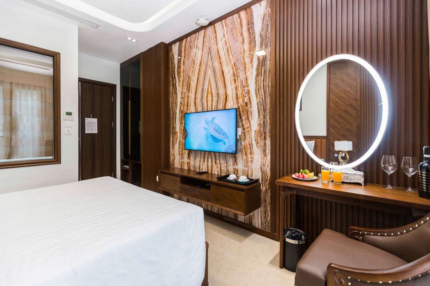 Habitación de hotel con cama, televisión instalada en una pared de mármol, tocador con espejo y una mesita con bandeja de desayuno.
