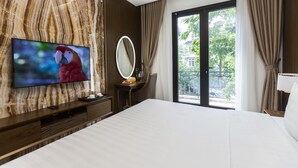 Une chambre d’hôtel moderne dotée d’un grand lit, d’un téléviseur fixé au mur en marbre, d’une table de chevet avec un miroir et offrant une vue sur l’extérieur grâce à une porte-fenêtre coulissante.
