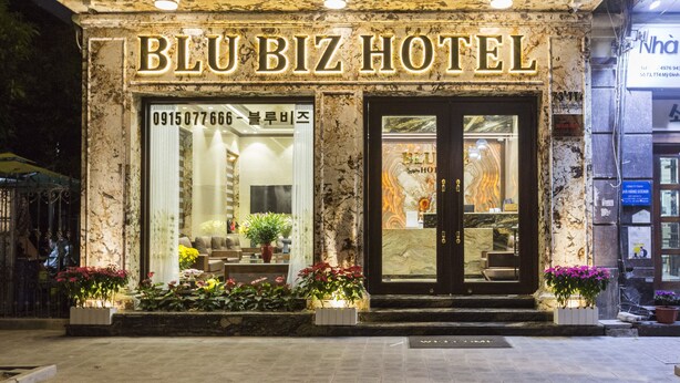 L’extérieur de l’hôtel BluBiz se distingue par sa façade en marbre, ses grandes fenêtres et les plantes en pot qui décorent l’entrée.