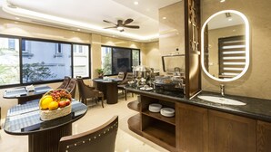 Une chambre d’hôtel moderne dotée d’un coin repas, d’une grande fenêtre, d’un ventilateur de plafond, d’un buffet et d’un grand miroir.