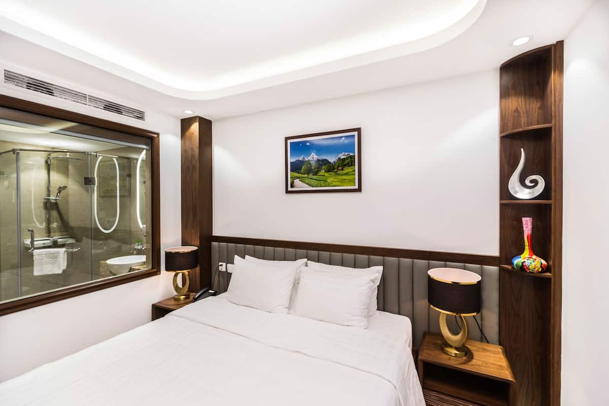 A hotel room with a bed, bedside tables, a mirror, a picture on the wall, and a shelf with decorative items.