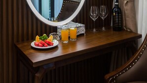 Une table en bois sur laquelle se trouvent un miroir rond, deux verres à vin, une bouteille de vin, une assiette de fruits et deux verres de jus d’orange.