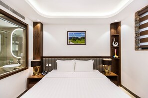 Een moderne hotelkamer met een groot bed, nachtkastjes met lampen, een grote spiegel en een ingelijst kunstwerk aan de muur.