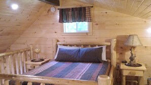 Camera da letto in una baita di legno, con un letto, un comodino, una lampada e una finestra con tende.