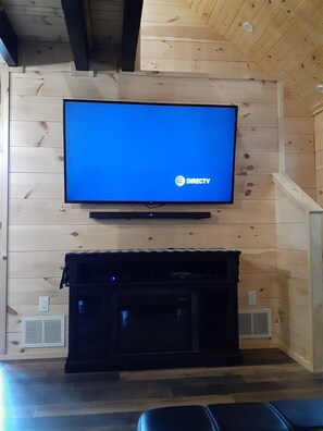 A flat-screen TV mounted on a wooden wall with a DIRECTV logo, a black entertainment unit below, and a wooden floor. - Turkey Trail, Hot Tub, Secluded, Pet Friendly (Logan)