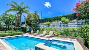 A rectangular swimming pool with a tiled deck, surrounded by palm trees and a stone wall with plants. - Luxury Renovation-Huge Upgrades! MustSee Pool -LED Games Room! Themed Rooms! (Reunion)