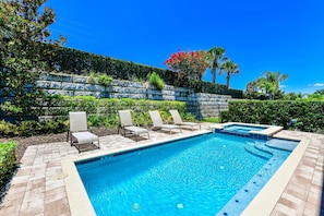 A swimming pool with lounge chairs, a stone retaining wall, and lush greenery.
