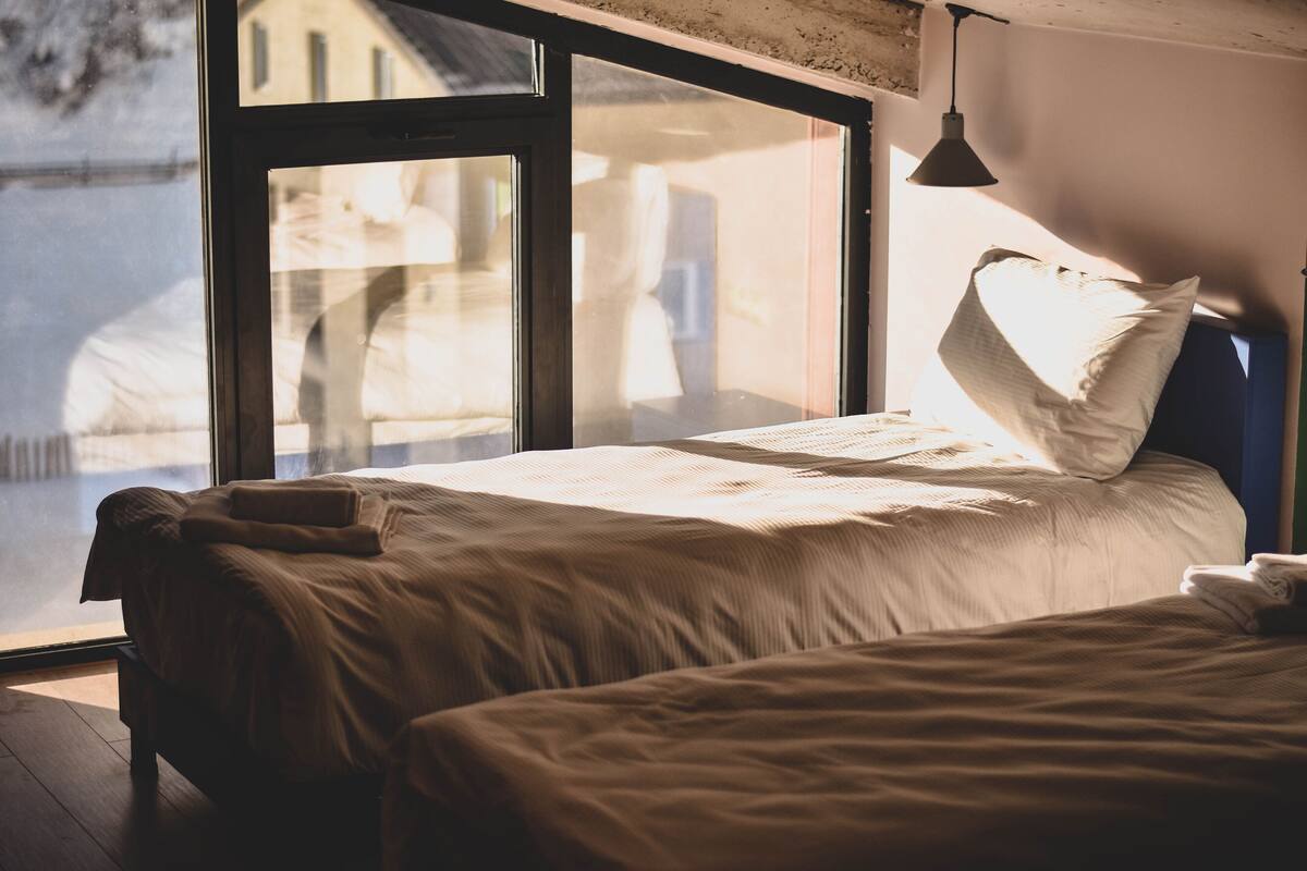 A bedroom with a large window, a bed, and a hanging light fixture.