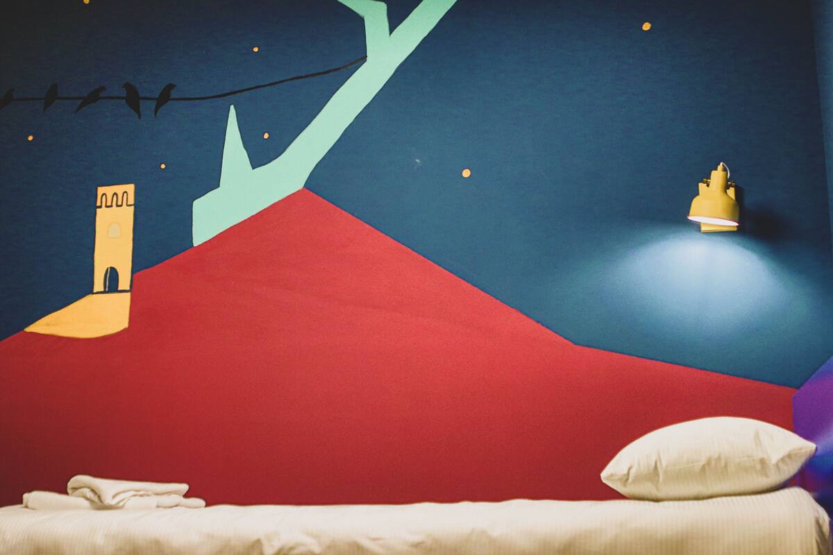 A room with a bed, a nightlight, and a mural of a castle on the wall.