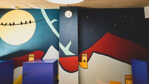 A room with a mural of a night sky, mountains, and a moon. There are blue cabinets and a white door. - Paliani Hostel (Mestia)