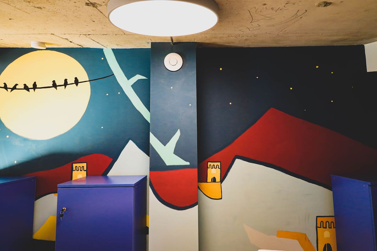 A room with a mural of a night sky, mountains, and a moon. There are blue cabinets and a white door.