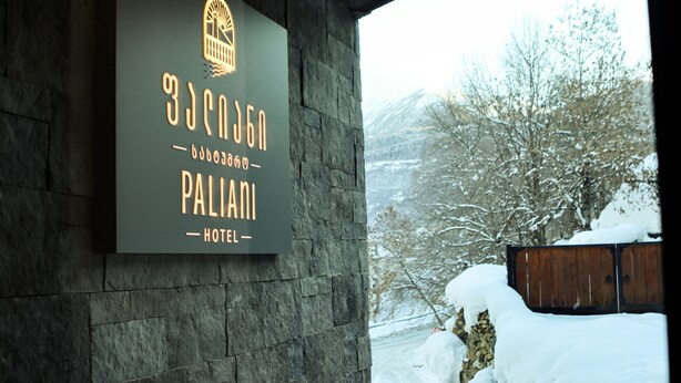 A sign for a hotel with a mountainous backdrop. - Paliani Hostel (Mestia)