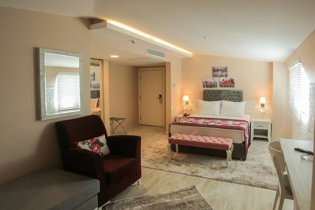Ein Schlafzimmer mit einem Bett, Nachttischen, einem Sessel, einer Bank, einem Schreibtisch und einem Spiegel.