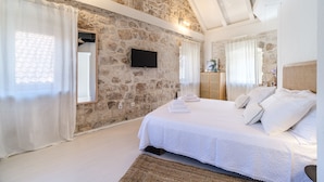 Un dormitorio con pared de piedra, televisor de pantalla plana, cama con ropa blanca y cabecera de madera.