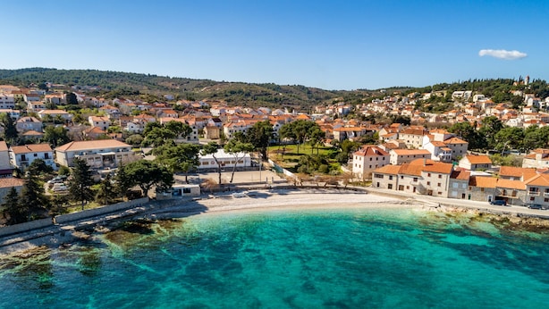 Un pueblo costero con playa, casas y una colina al fondo.