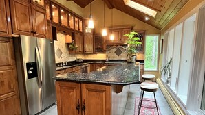 A spacious kitchen with wooden cabinets, a stainless steel refrigerator, and a large island with stools.