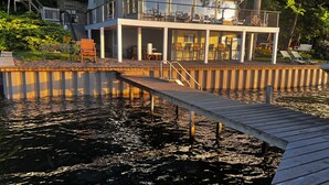 Ein Ufergrundstück mit Anlegesteg, einer überdachten Terrasse mit Sitzgelegenheiten und einer Treppe zum Obergeschoss.